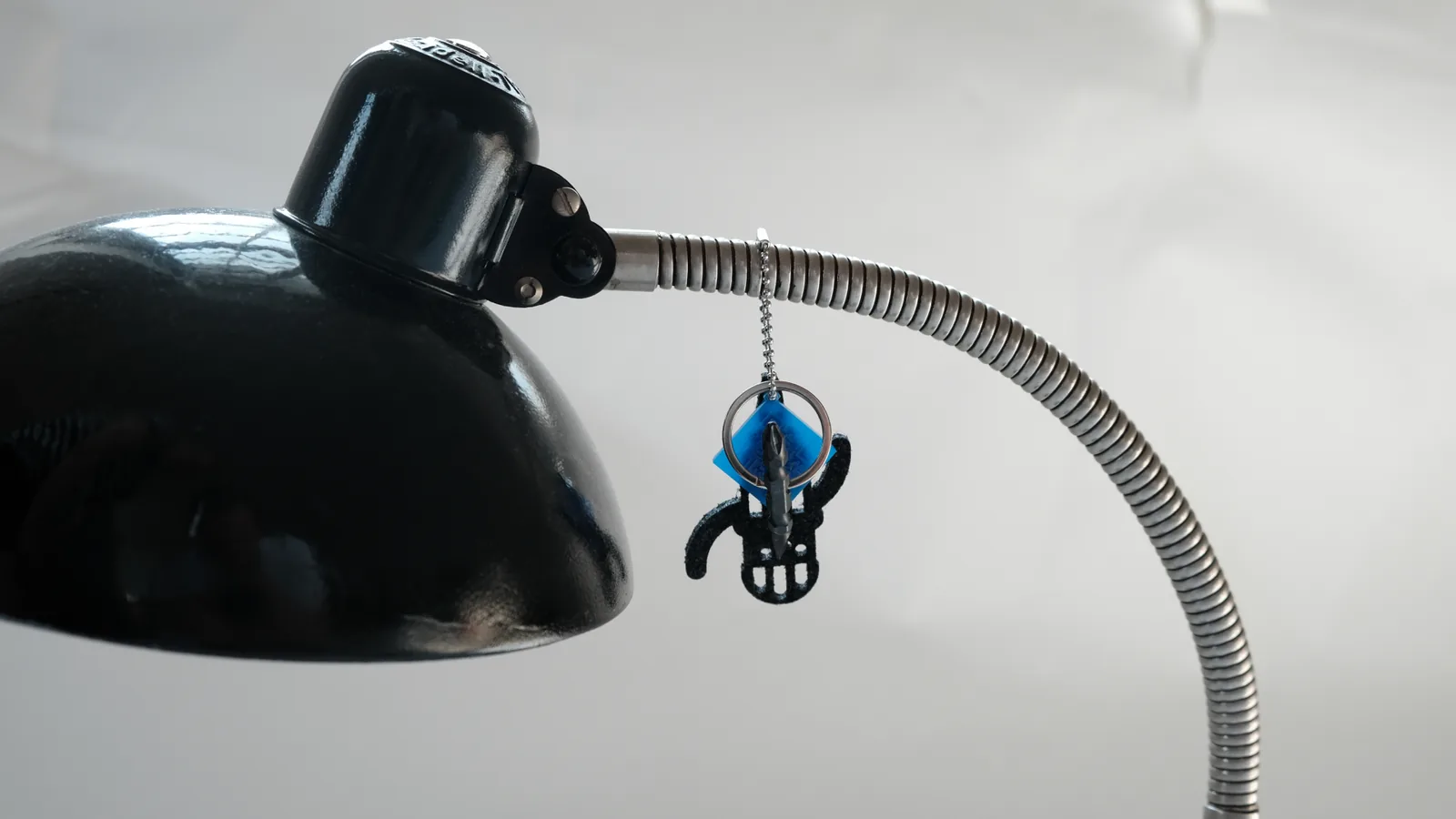 Eine schwarze Schreibtischlampe, am Hals hängt ein gedrucktes Figürchen mit blauem QR-Anhänger.