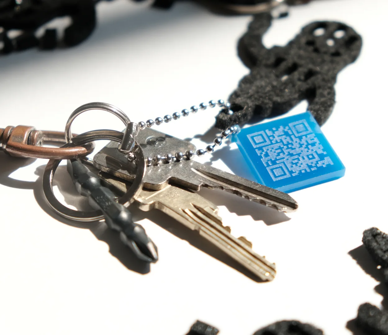 Ein Schlüsselbund mit einem gedruckten schwarzen Figürchen und einem blauen QR-Anhänger.